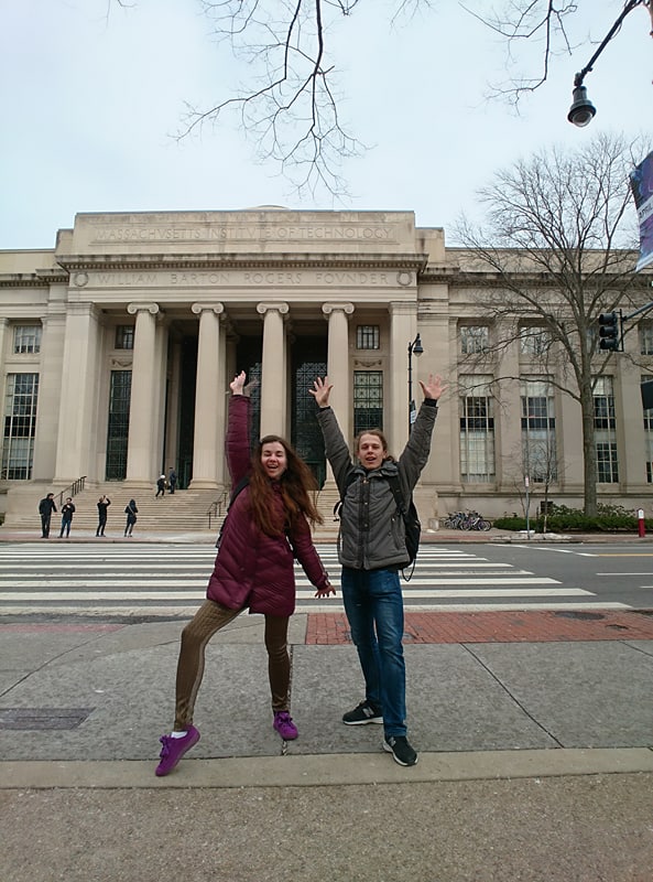 Roman and Olena are both in front of the MIT Rogers building with their hands up in the air looking happy.