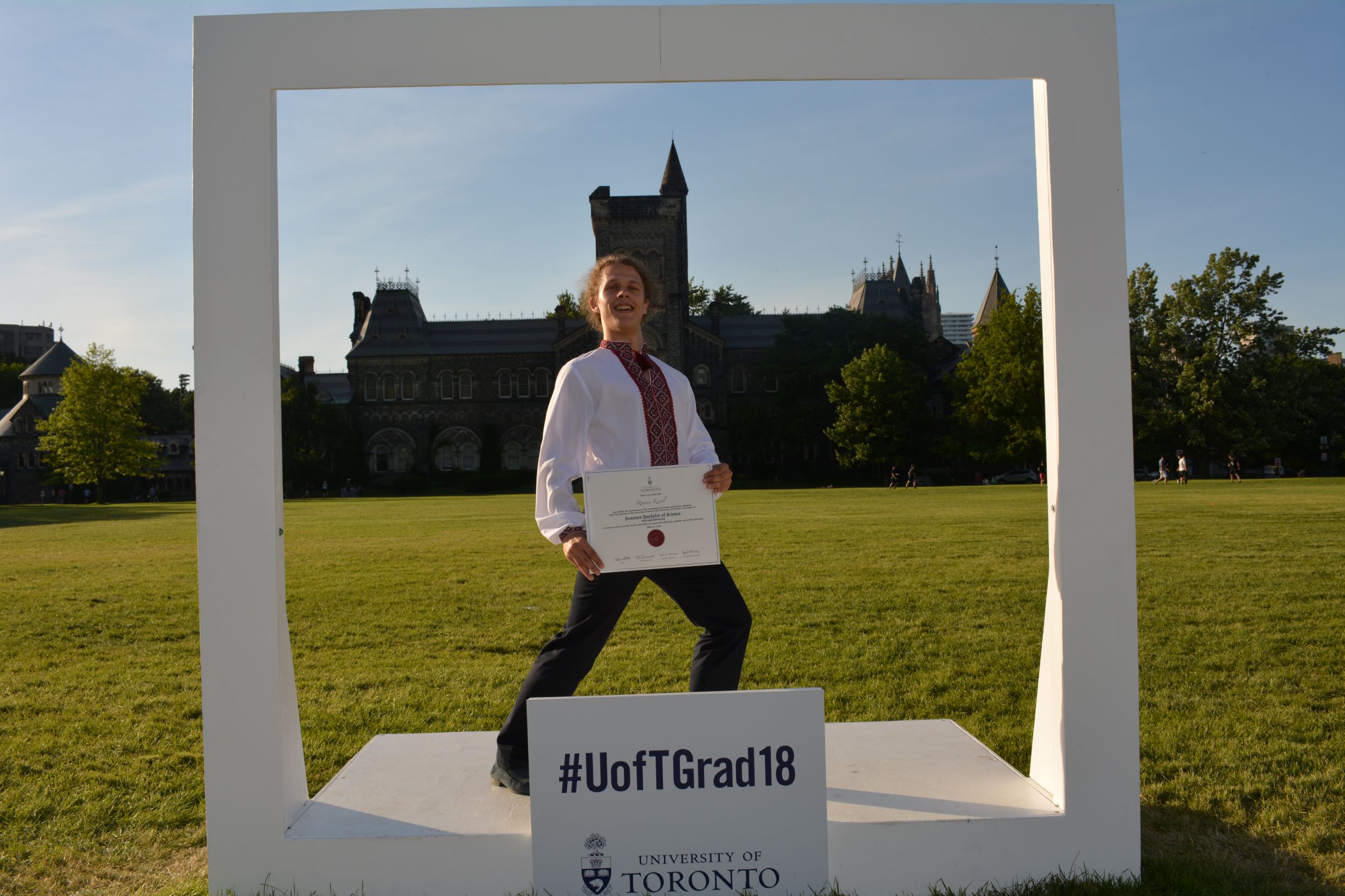 Roman inside a life sized picture frame around the University college tower of the University of Toronto. He is holding his Bachelors diploma.